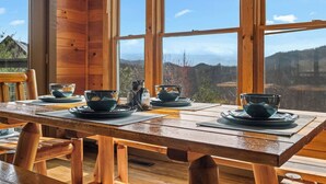A wooden dining table set with bowls and plates, large windows, and a view of the outdoors. - 1 Great Mountain View-3 Bed Cabin in Wears Valley (SEVIERVILLE)