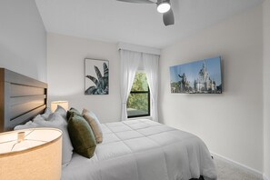 A bedroom with a bed, a ceiling fan, a window with curtains, and two wall-mounted paintings. - 5BD/5BA Family Home with Pool & Game Room (Orlando)