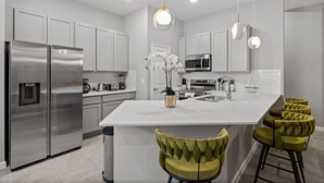 Una cocina moderna con electrodomésticos de acero inoxidable, una isla central y taburetes de bar tapizados en verde.