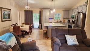 A modern living room with a sofa, a dining area with a table and chairs, and a kitchen with cabinets and appliances.