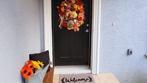 A front door with a wreath, a welcome mat, and a small table with flowers.