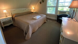 Un dormitorio con cama, mesitas de noche, lámpara, silla y ventana con persianas.