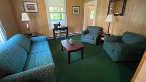 Una sala de estar con dos sofás azules, una mesa de centro de madera y dos sillones. Hay cuadros enmarcados en las paredes y un espejo sobre los sillones.