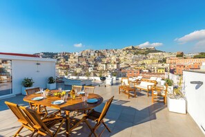 A rooftop terrace with a dining table set for four, surrounded by wooden chairs, overlooking a densely packed cityscape with historic buildings. - Poerio Rooftop Luxury Apartment (Naples)