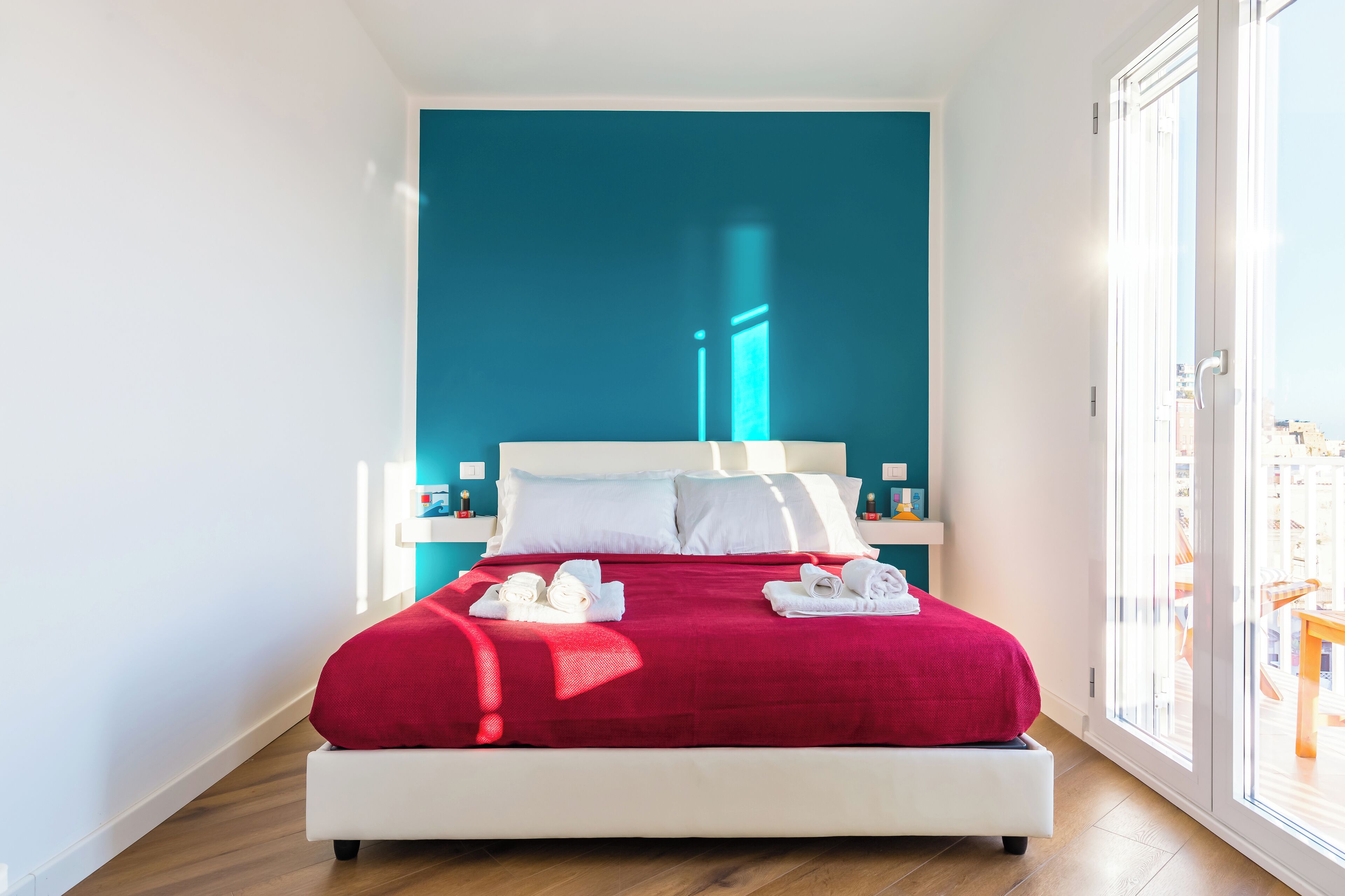 Ein modernes Hotelzimmer mit einem großen Bett, weißer Bettwäsche und einer roten Decke.