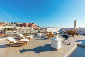 Una terraza en la azotea con sillones de descanso, una parrilla y un comedor con mesa y sillas.