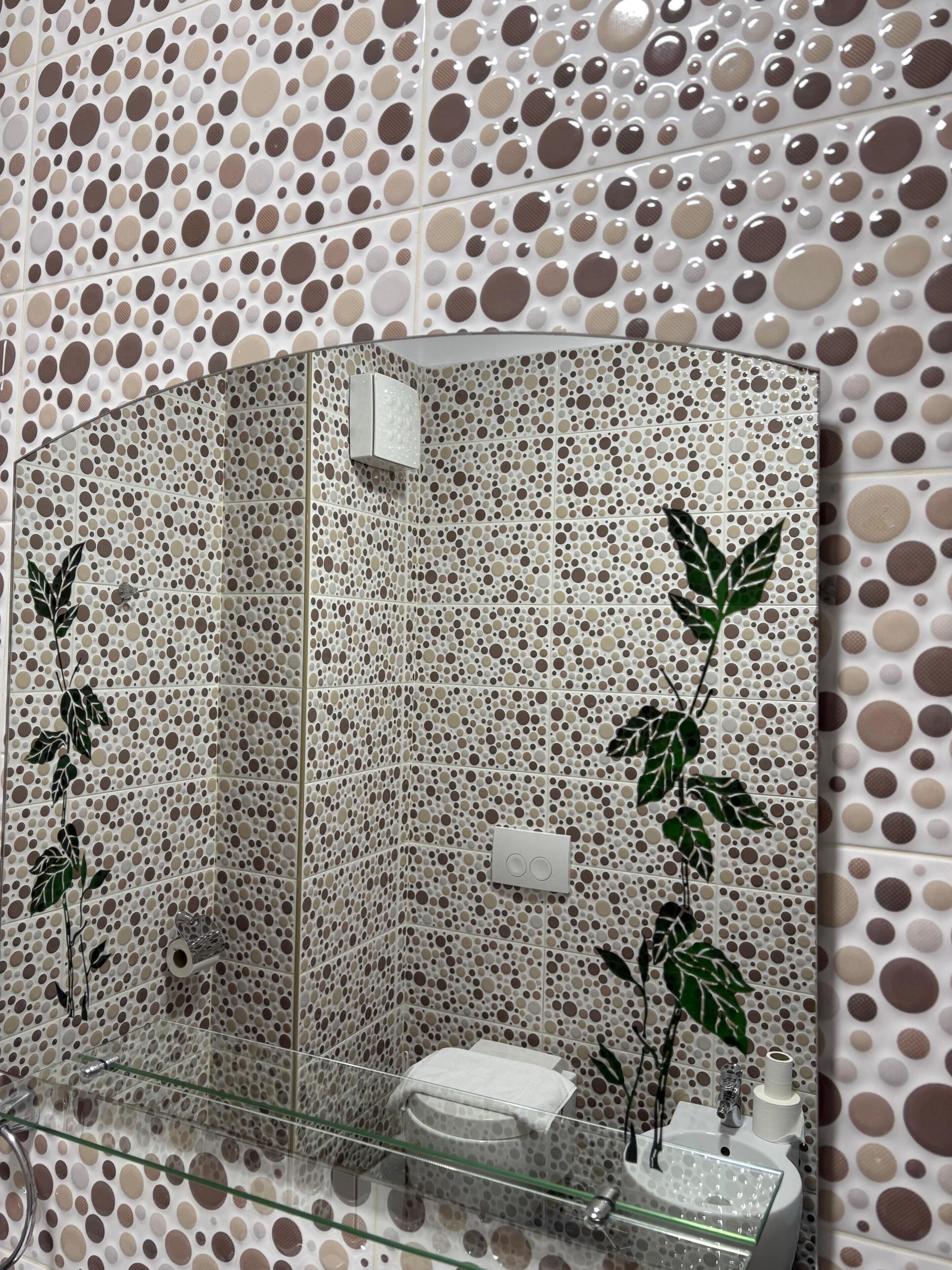 A bathroom with a polka dot tile pattern, a glass shower enclosure, and a glass sink with a mirror.