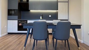 Eine moderne Küche mit integrierten Geräten, ein Essbereich mit einem dunkelholztischen Tisch und Stühlen sowie ein schlichtes Decken-Design.