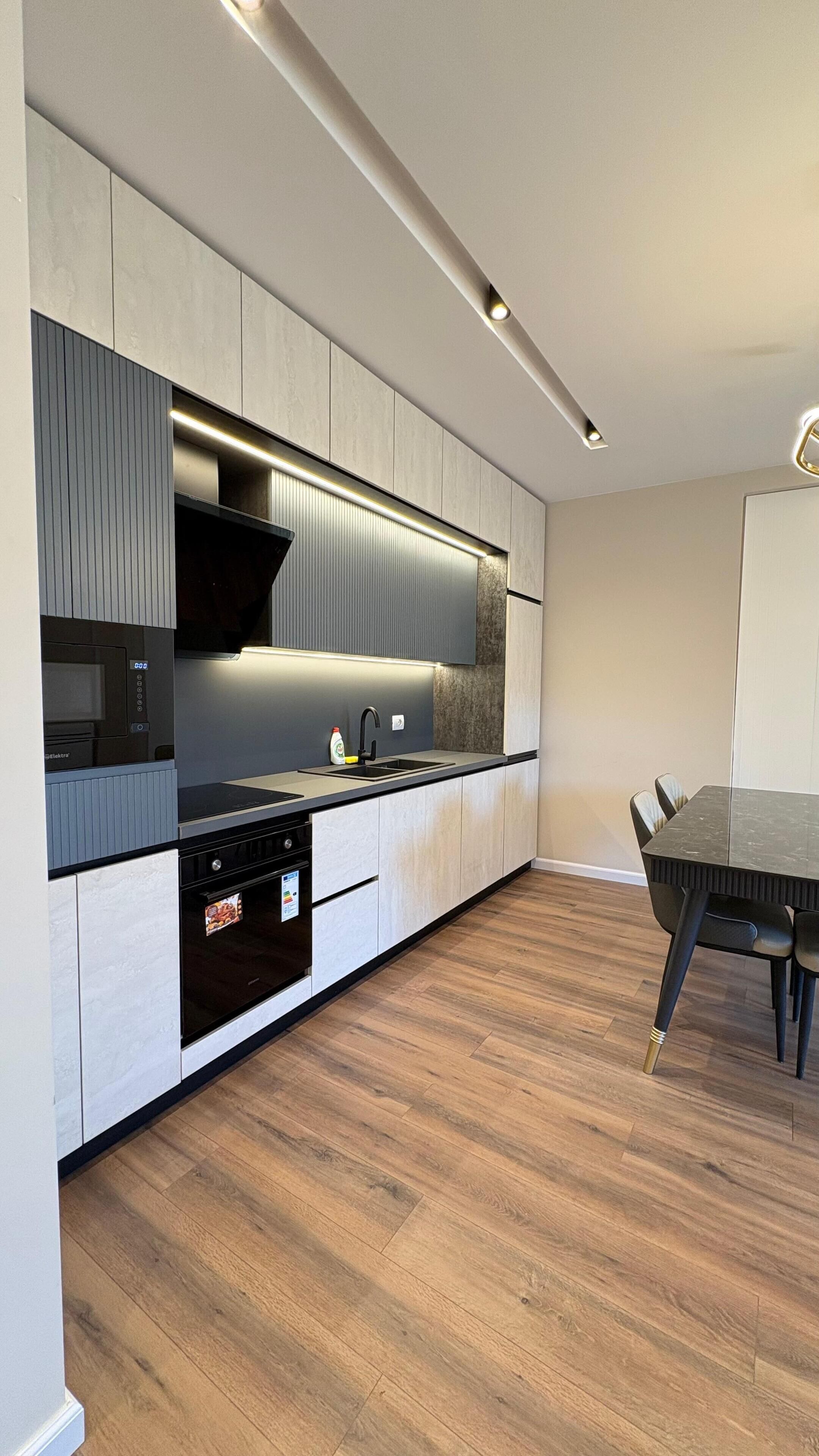 Una cocina moderna con electrodomésticos integrados, un comedor con mesa y sillas, y piso de madera.