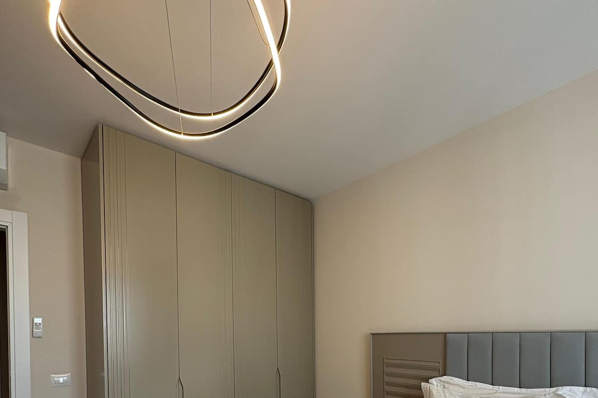 A bedroom with a bed, a grey wardrobe, and a modern ceiling light fixture.
