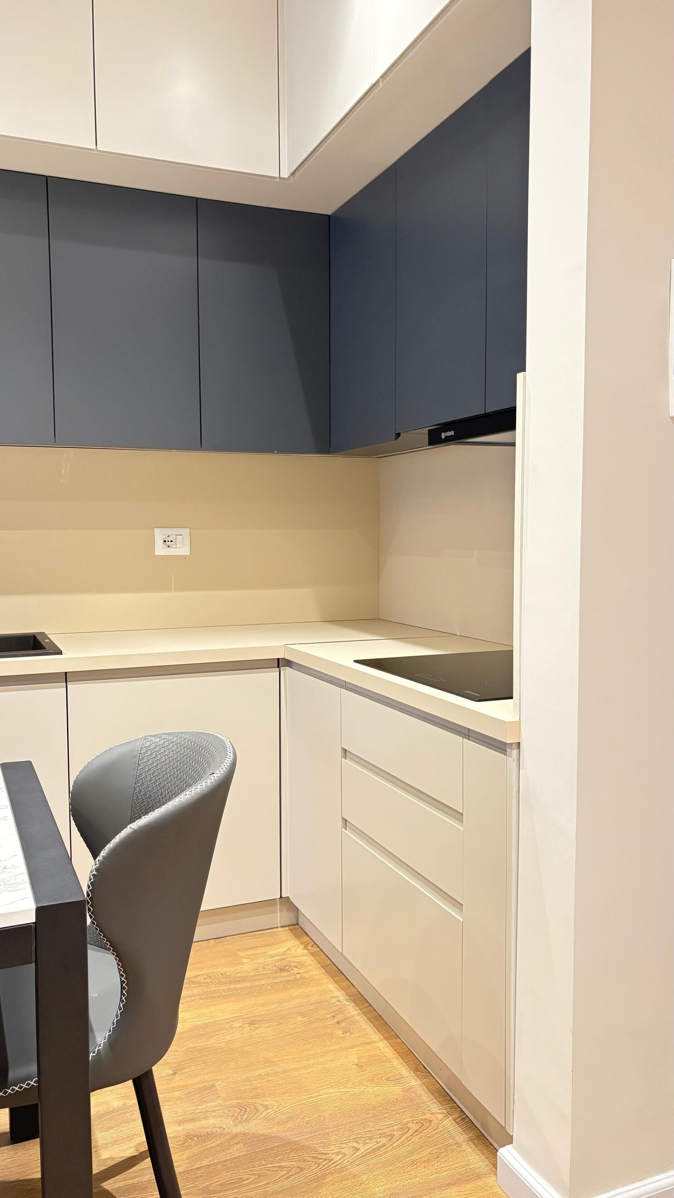 A compact kitchen with white and dark blue cabinets, a black countertop, and a grey chair.