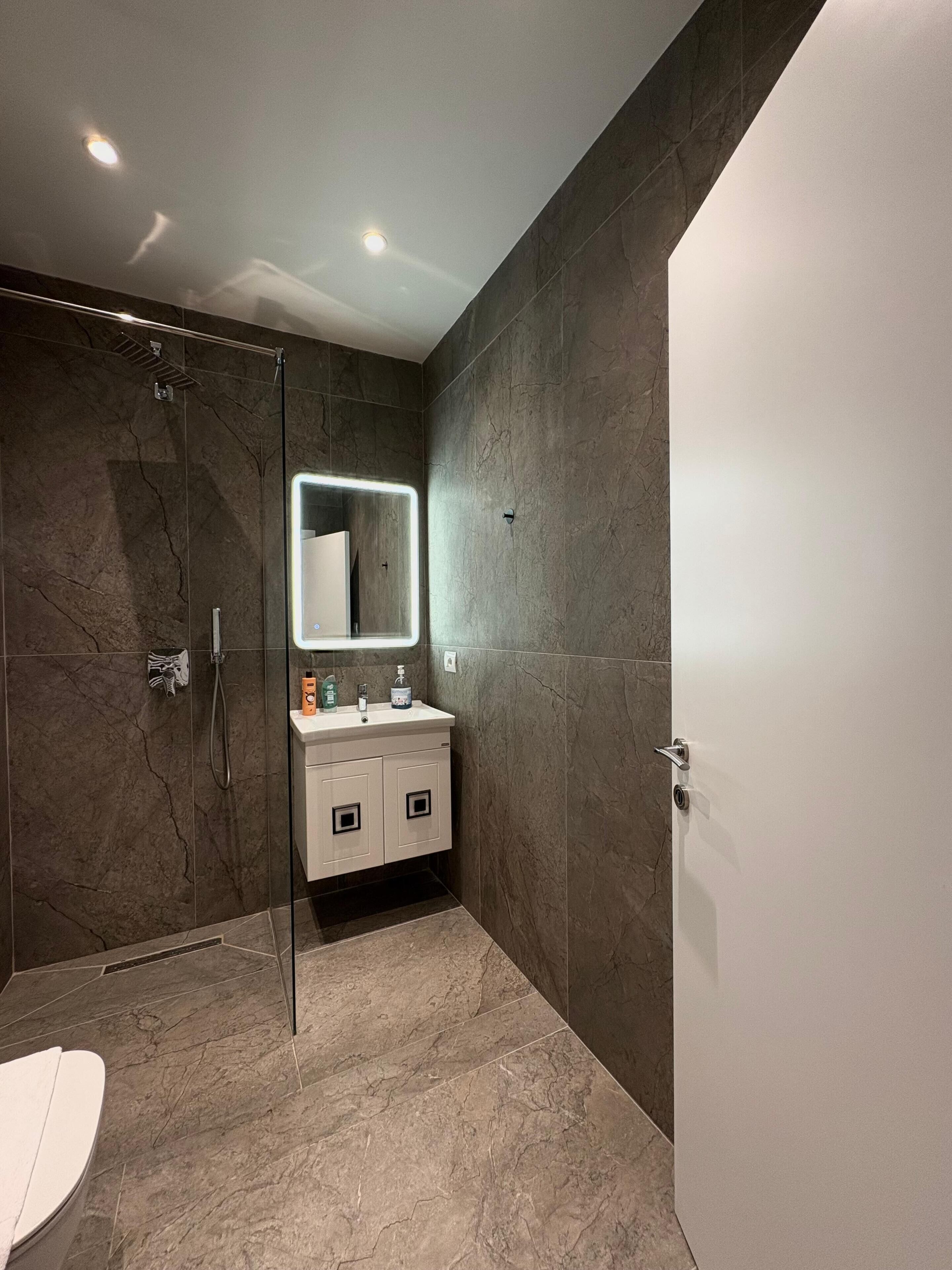 A modern bathroom with a glass-enclosed shower, a white sink with a mirror, and a white toilet.