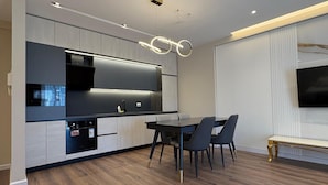 Eine moderne Küche mit integrierten Geräten, ein Essbereich mit Glastisch und ein Wohnbereich mit Fernseher.