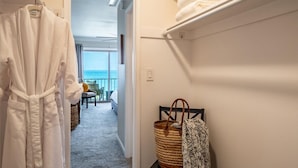 A hotel hallway with a white robe hanging on a rack, a wicker basket, and a bench with a patterned throw. A balcony with a view is visible in the background. - SeaCliff - Harbor View - Oceanfront Luxury in Santa Barbara (Santa Barbara)