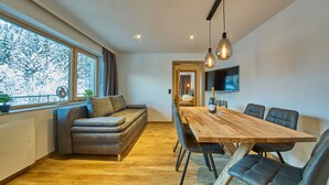 Un espace repas moderne avec une table et des chaises en bois, un canapé et un téléviseur fixé au mur.