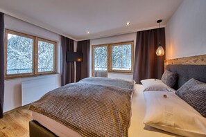 Een slaapkamer met een groot bed, twee ramen met gordijnen, een televisie aan de muur en een houten hoofdbord.