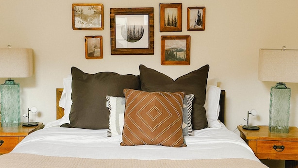 A neatly made bed with a white comforter and multiple pillows, flanked by two bedside tables with lamps and framed pictures on the wall above. - Mountain Views, 3BR, HotTub & Ski Access (Crested Butte)