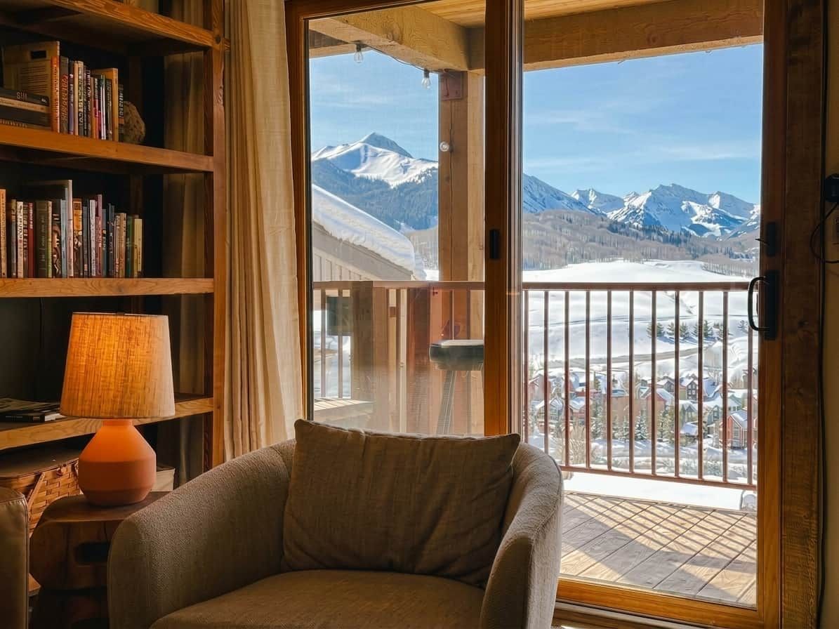A cozy room with a large window overlooking a snowy mountain landscape.
