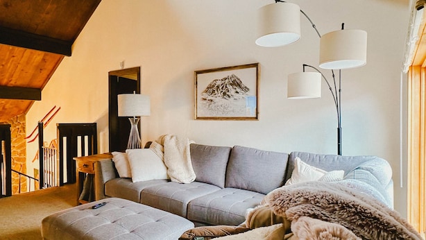 A living room with a grey sofa, a matching ottoman, a floor lamp, a framed picture on the wall, and a staircase with a wooden railing. - Mountain Views, 3BR, HotTub & Ski Access (Crested Butte)