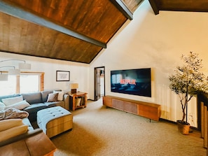 A living room with a sofa, a coffee table, a TV mounted on the wall, a potted plant, and a framed quote on the wall.