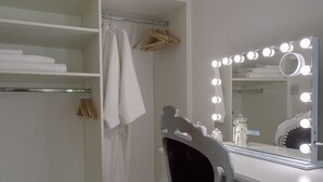 Une coiffeuse avec un miroir entouré de lumières, une chaise et une étagère avec des serviettes pliées.