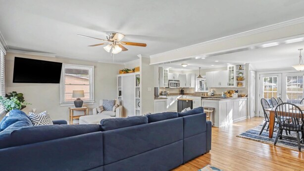 A modern living room with a dark blue sectional sofa, a dining area with a wooden table and chairs, and a kitchen with white cabinets and a central island. - Parris Island 10 min - Pet friendly Home + Yard (Beaufort)