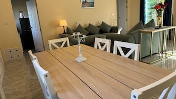 A dining area with a wooden table, white chairs, a candelabra, and a green sofa in the background.