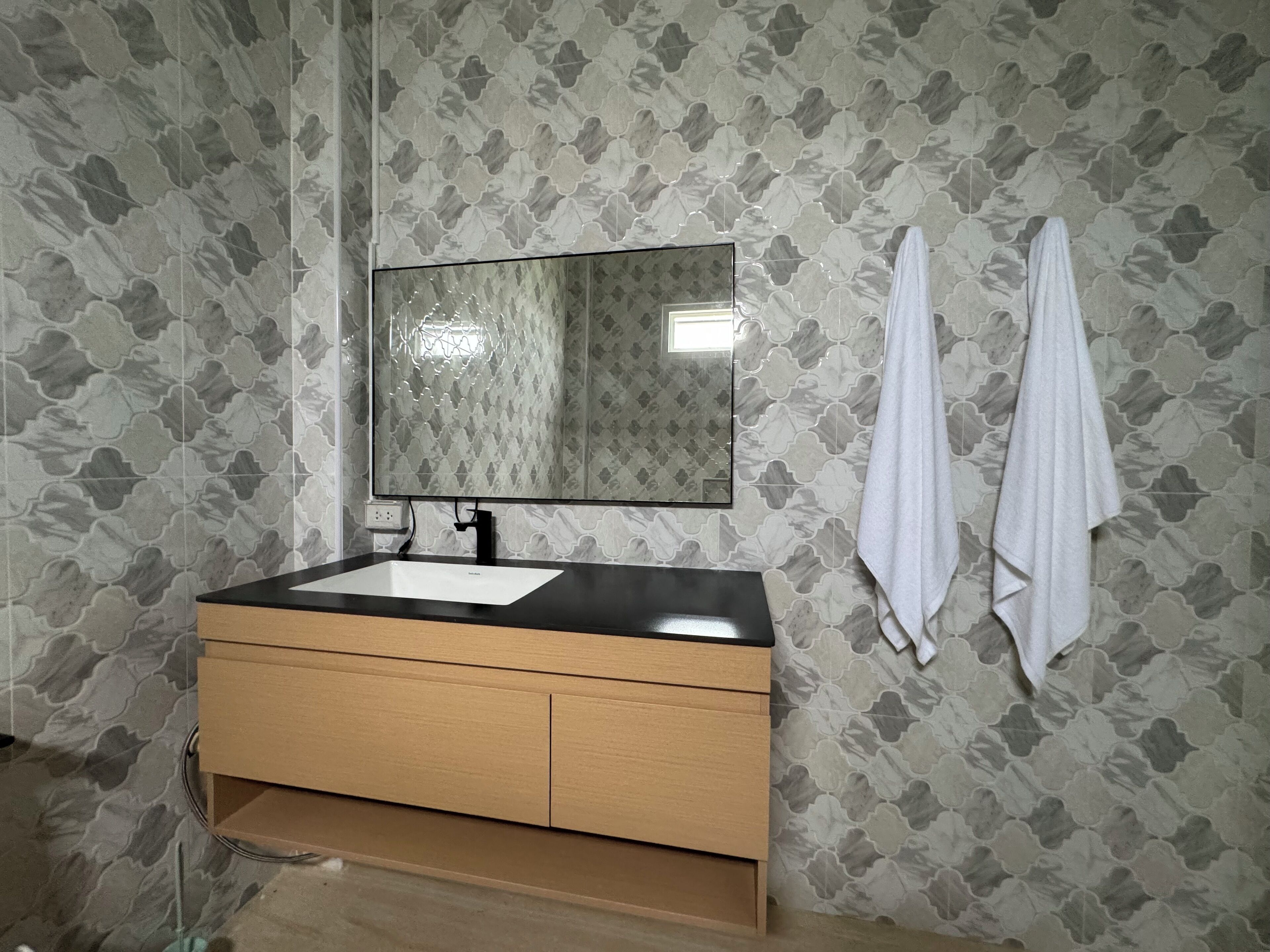 A bathroom with a wooden vanity, a white sink, and a mirror. There are two white towels hanging on the wall.