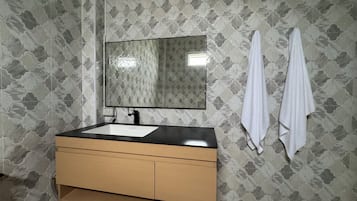 A bathroom with a wooden vanity, a white sink, and a mirror. There are two white towels hanging on the wall.