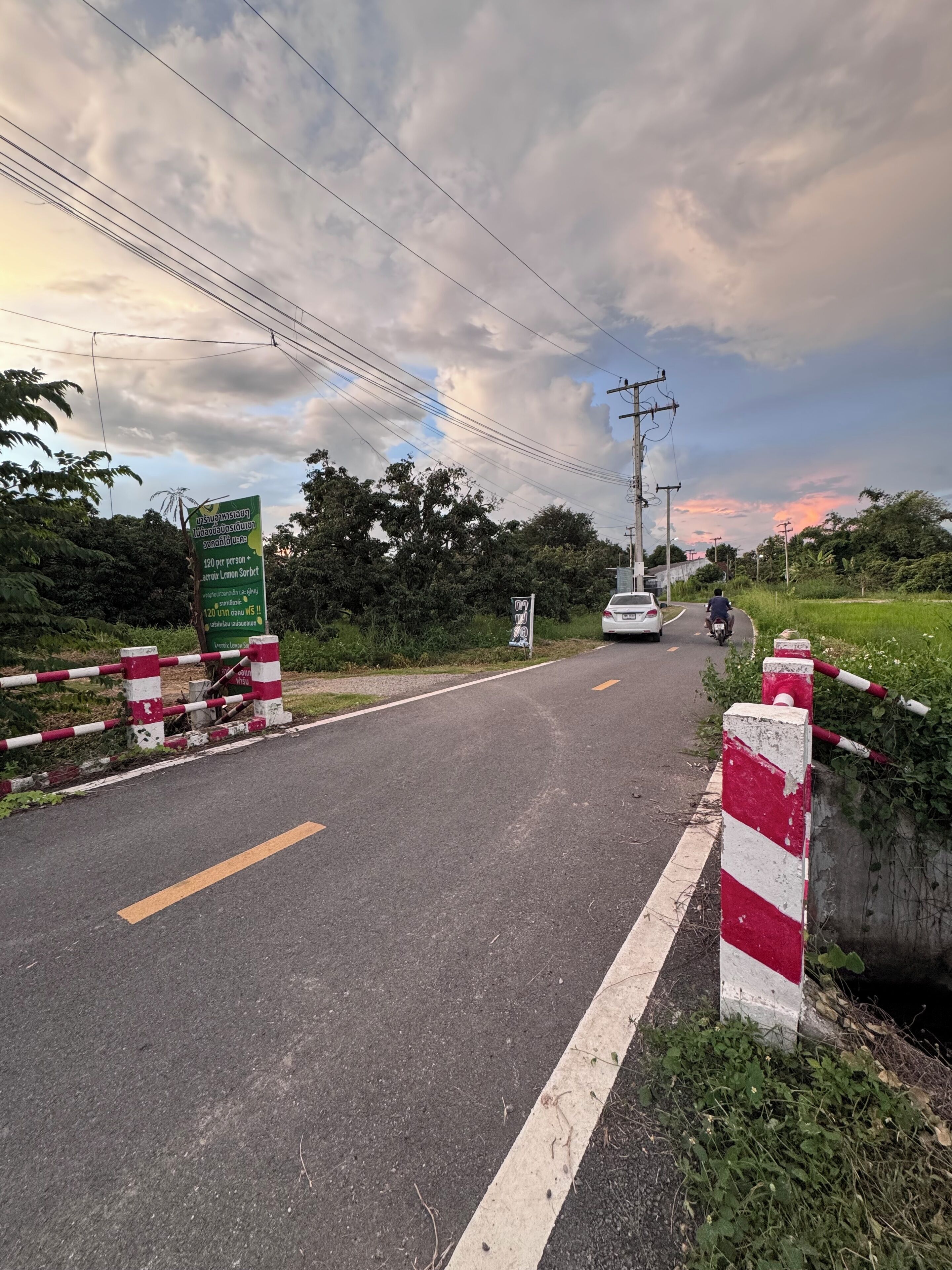 A rural road with a red and white striped barrier, a white car, and a motorbike.