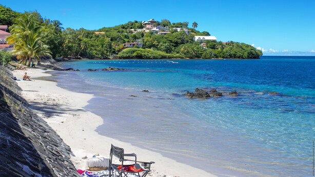 A beach with clear blue water, a chair, and a blanket on the sand. - Horizon Bleu (Trois-Ilets)