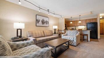 A living room with a sofa, armchairs, a coffee table, and a dining area with chairs and a kitchen in the background.
