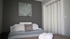 Een slaapkamer met een bed, kussens, een deken en opgerolde handdoeken op het bed.