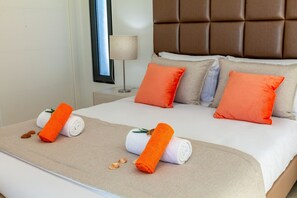 A neatly made bed with two orange towels and a white towel, a brown headboard, and a window with a lamp on the side. - Villa Aqua 3 (Albufeira)