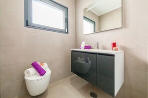 A modern bathroom with a toilet, a sink, a mirror, and a window. - Villa Aqua 3 (Albufeira)