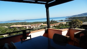 Un balcon avec une table et des chaises, donnant sur un paysage côtier avec des bâtiments et de la végétation.