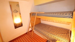 Une chambre avec un lit superposé, une échelle, un miroir et une petite table de chevet.