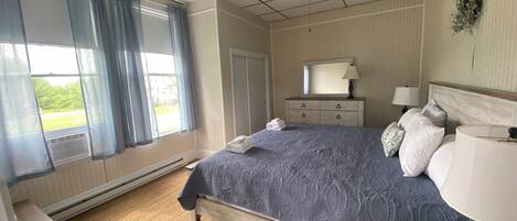 Ein Schlafzimmer mit Bett, Schminktisch, Nachttisch, Deckenventilator und einem Fenster mit Vorhängen.