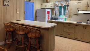 Una cocina con armarios de madera, una puerta azul, un refrigerador, un fregadero y una zona con taburetes de bar.