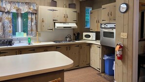 Una cocina con armarios de madera, un microondas, un horno, un lavabo y un reloj en la pared.