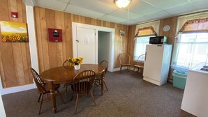 A dining area with a wooden table and chairs, a white refrigerator, and a microwave.