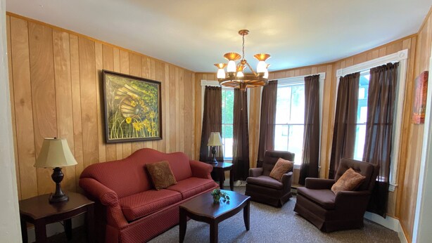 A living room with a red sofa, two armchairs, a coffee table, a chandelier, and a painting on the wall.