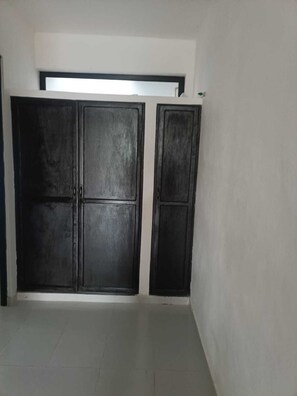 Spacious room with a large wardrobe, tiled floor, and a small window.