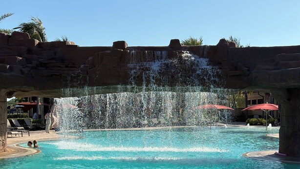 Une piscine agrémentée d’une cascade, entourée de chaises longues et de parasols.