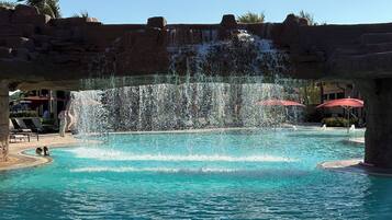 A pool with a waterfall feature, surrounded by lounge chairs and umbrellas.