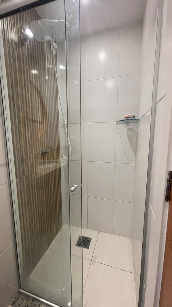 Un box de ducha con paredes de vidrio, suelo de azulejos y puerta de cristal.