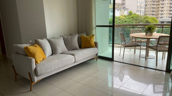 Una sala de estar moderna con un sofá gris, cojines amarillos y vistas a un balcón con mobiliario exterior.