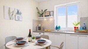 Une cuisine moderne avec une table à manger pour quatre personnes, des meubles blancs, une fenêtre offrant une belle vue et des œuvres d’art décoratives sur les murs.