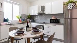 Une cuisine moderne avec des meubles blancs, un réfrigérateur en acier inoxydable et une table à manger pour quatre personnes.