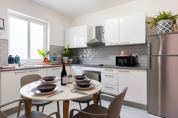 Una cocina moderna con armarios blancos, un refrigerador de acero inoxidable y una mesa de comedor para cuatro.